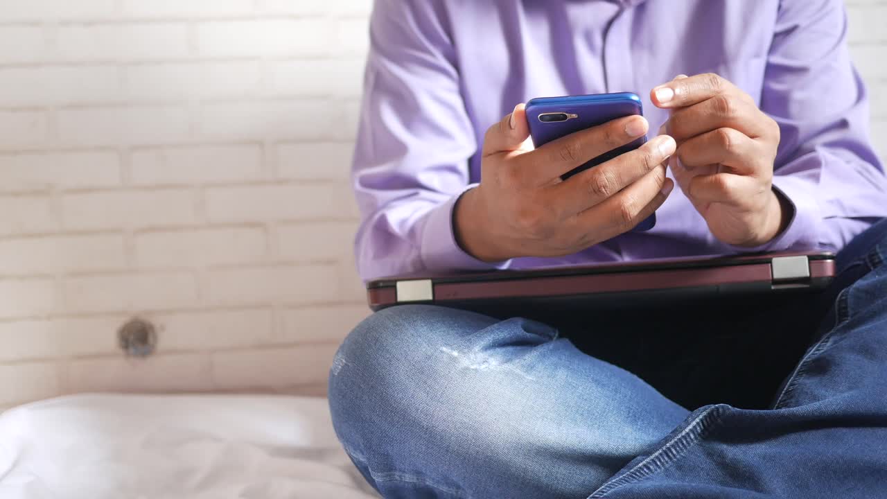 persona que usa un teléfono inteligente y una computadora portátil mientras está sentada en una cama.