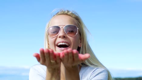 beautiful young blonde blows holi colorful powder off her hands and laughs. clear blue sky behind her.