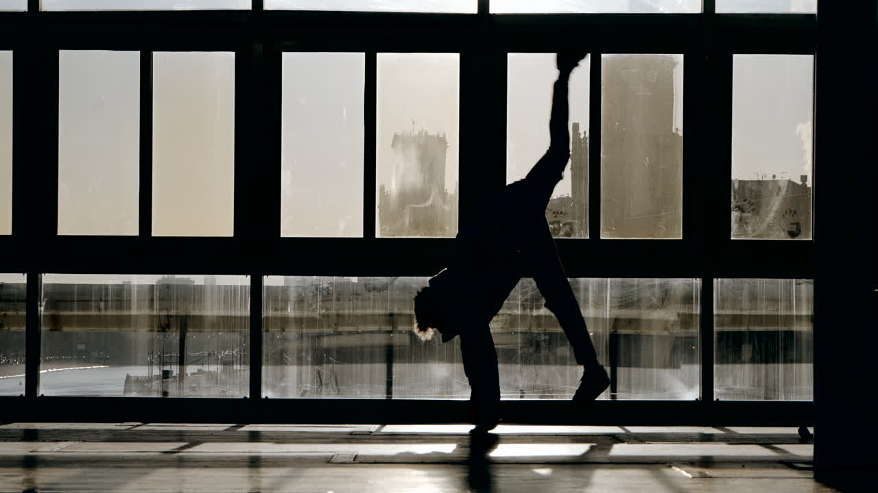 Silhouette of a person performing action in a urban setting with large windows