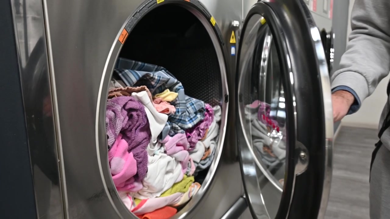 Man Opening an Industrial Washing Machine in a Self-Service Laundromat
