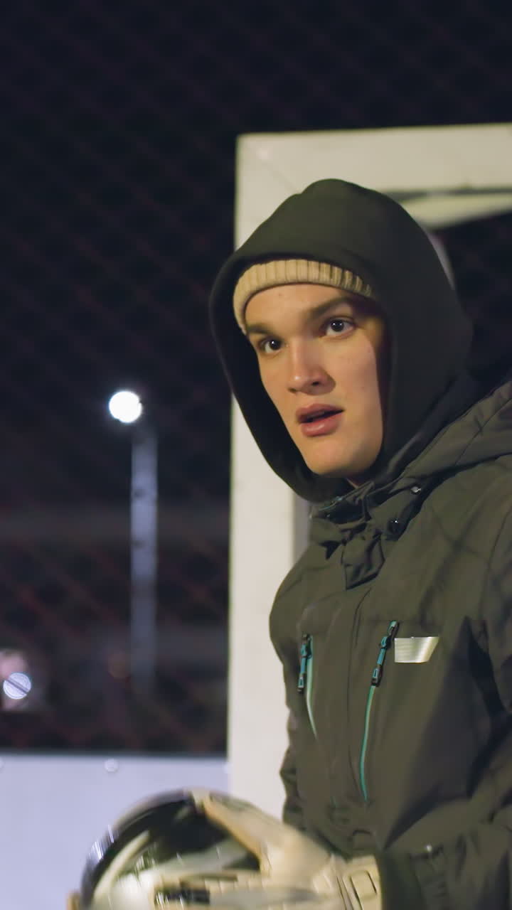 atleta con capucha y gorra rebota la pelota de fútbol una vez antes de patearla con precisión durante la sesión de entrenamiento bajo un telón de fondo urbano iluminado