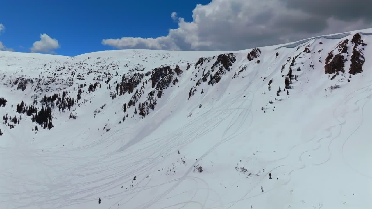 Snowmobile Montezuma Deer Creek winter spring deep backcountry powder snow aerial drone Colorado avalanche terrain cornice chute tracks Rocky Mountain peaks sunny blue skies clouds pan up forward