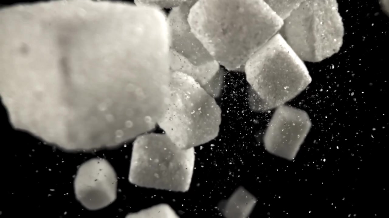 Hvite sukkerbiter faller i sakte film på svart bakgrunn