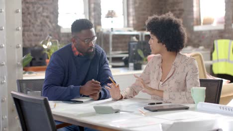 diverse architect colleagues discussing work at table with blueprint in slow motion