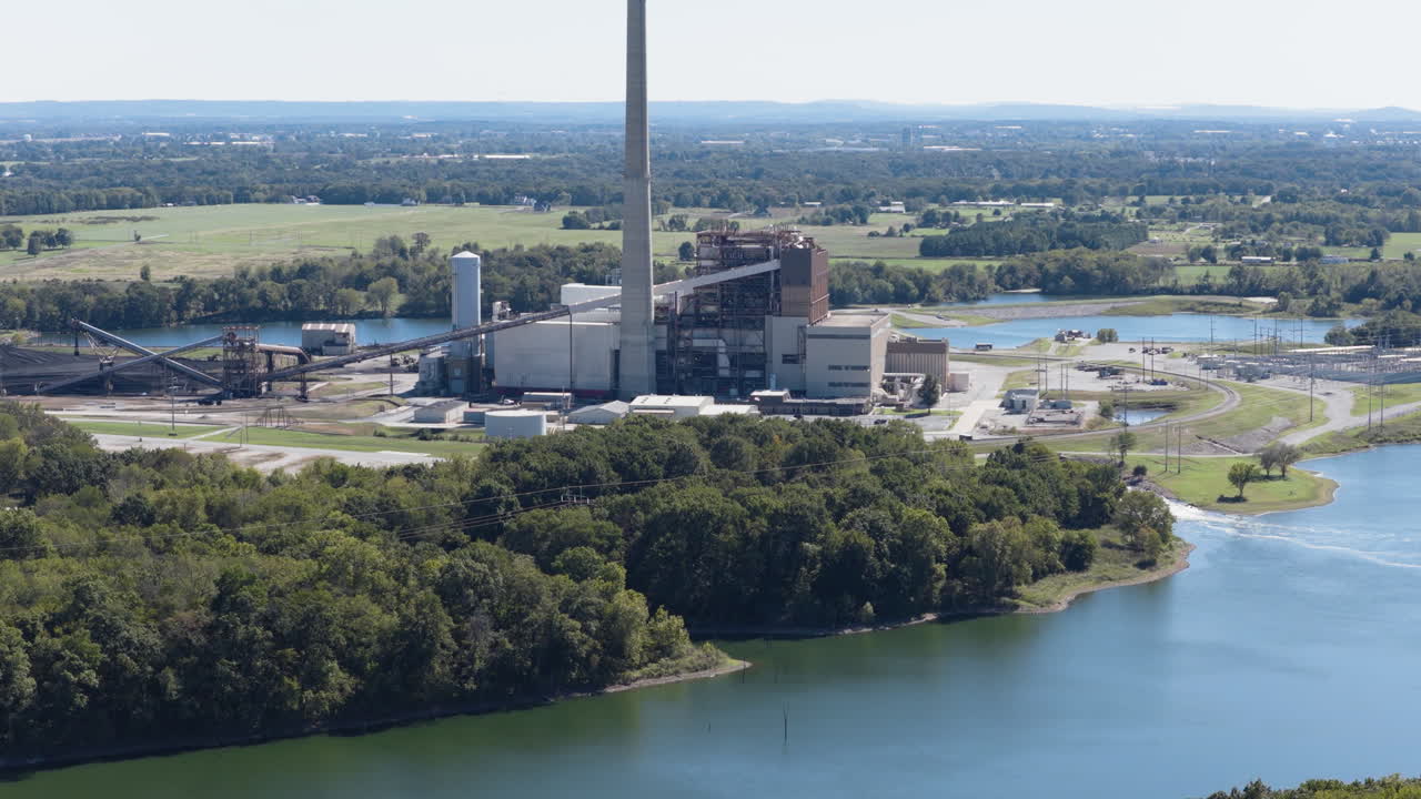 River bend with power facilities and wooded banks bordering calm water, aerial establishing tracking left tilt up