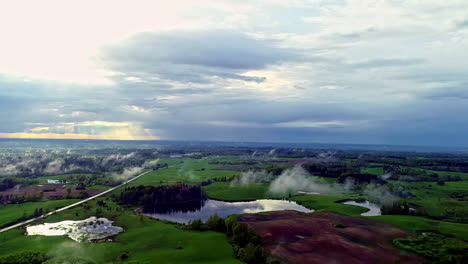 Aerial-backward-moving-shot-of-a-road-passing-through-beautiful-rural-landscape-with-small-lakes-visible-ona-cloudy-day