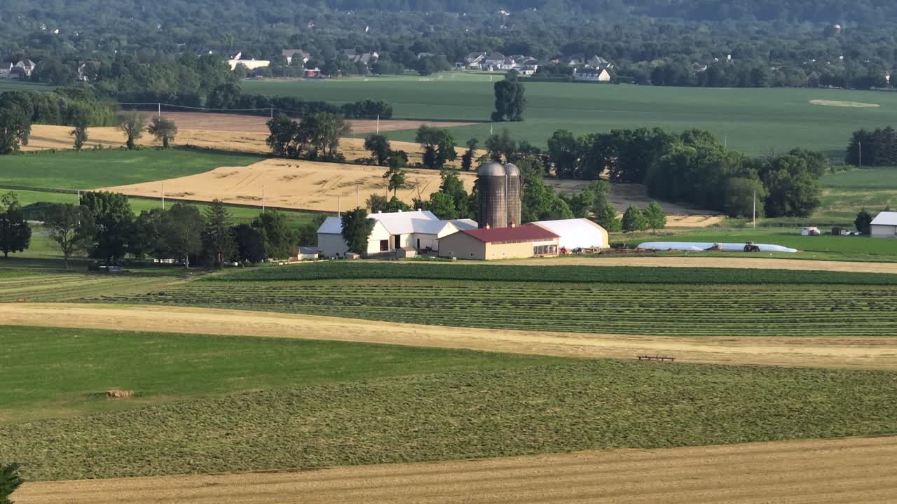 Drone vidvinkelbillede af pæn bondegård med to siloer ved solnedgang. Ejendom i landområde med bakker og bjerge i det fjerne. Lader og stald til husdyr