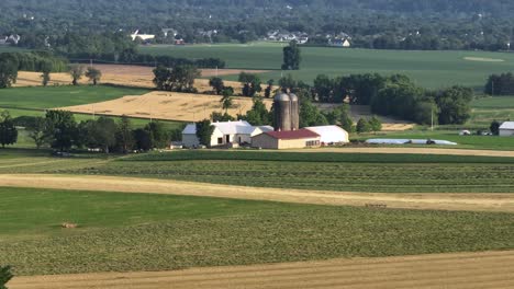 drone wide shot of neat farmstead with two silo storages at sunset time. real estate in rural area with hills and mountains in distance. barns and stable of livestock