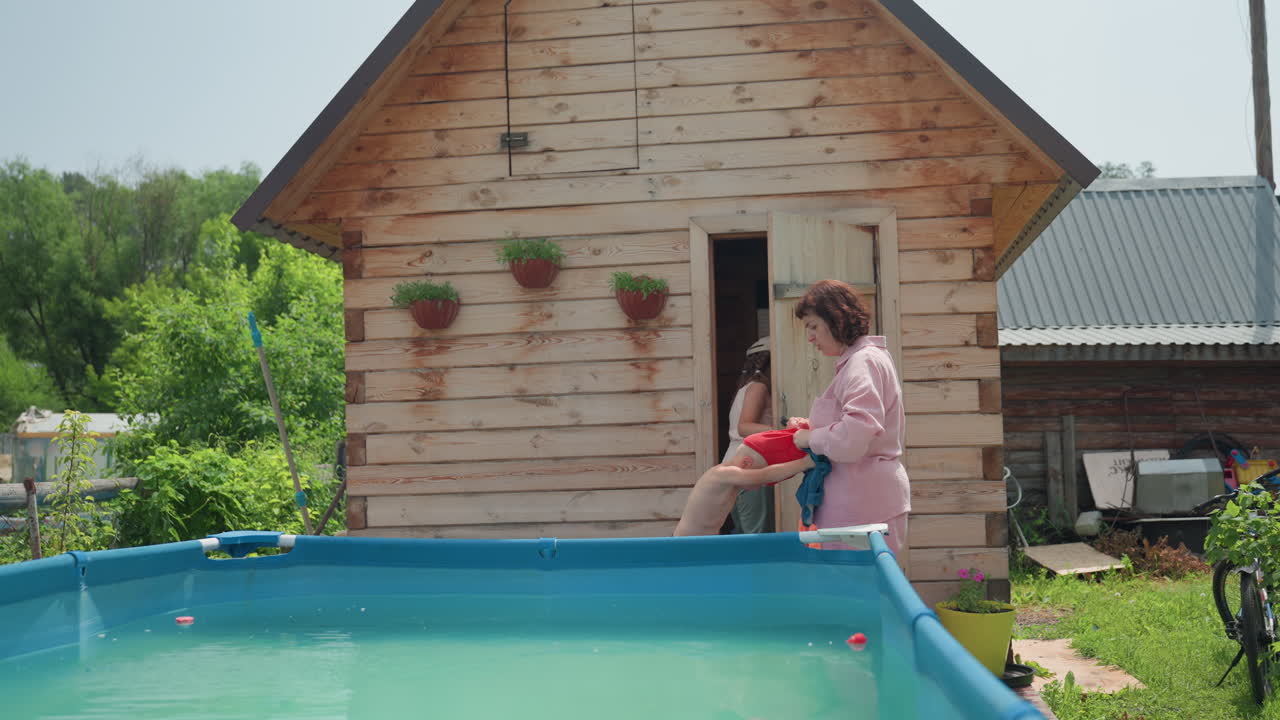 Older Lady Guides Toddler Into Water, Senior Woman Gently Supports Toddler In Summer Backyard Fun, Elderly Grandmother Helps Small Child Into Pool During Bright Sunny Outdoor Day At Home