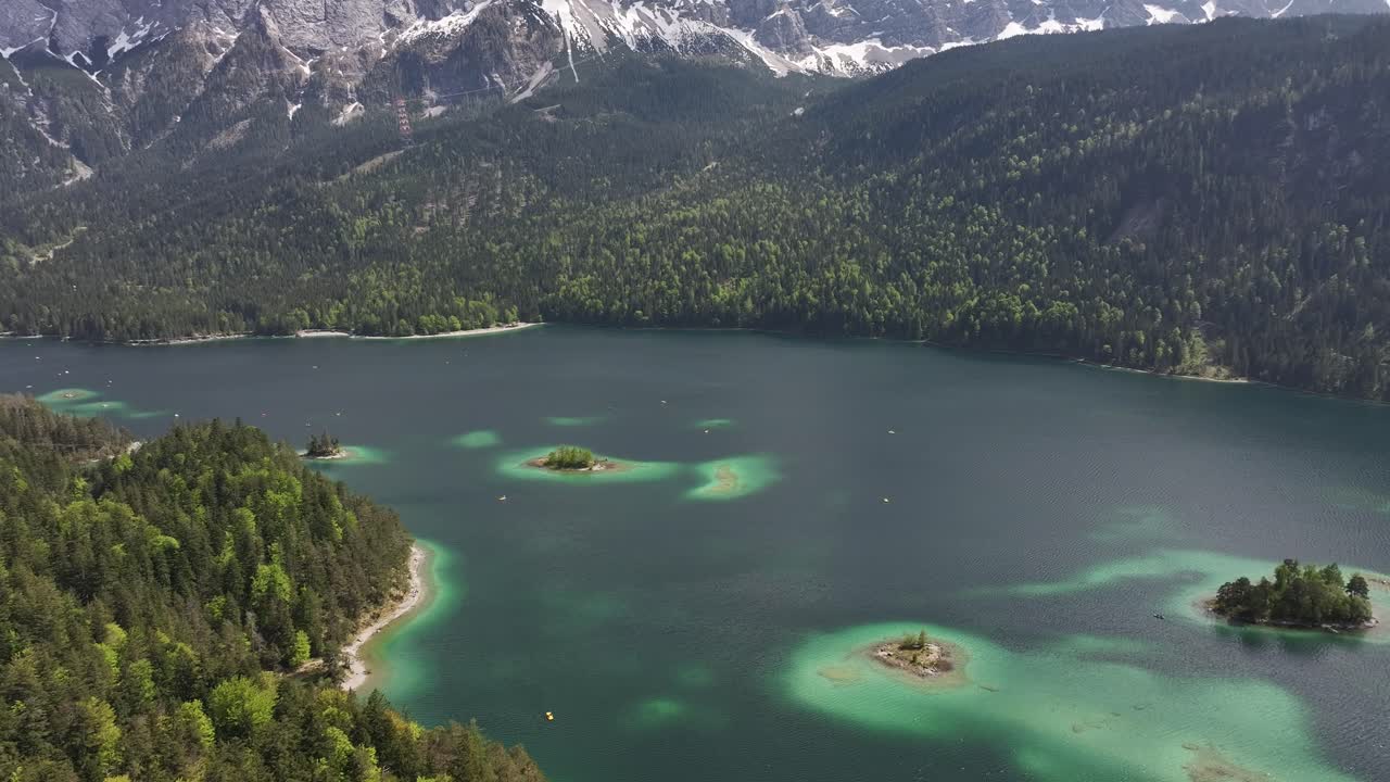 las aguas claras turquesas de eibsee, las pequeñas islas y los densos bosques con un telón de fondo de montañas cubiertas de nieve en grainau, alemania