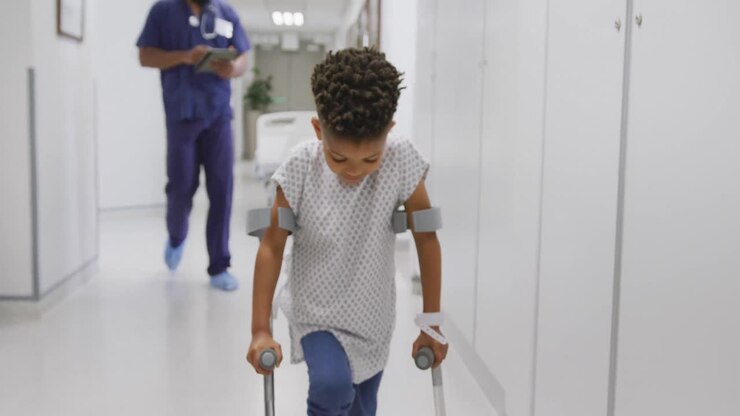 médecin afro-américain marchant avec un enfant patient en utilisant des béquilles à l'hôpital