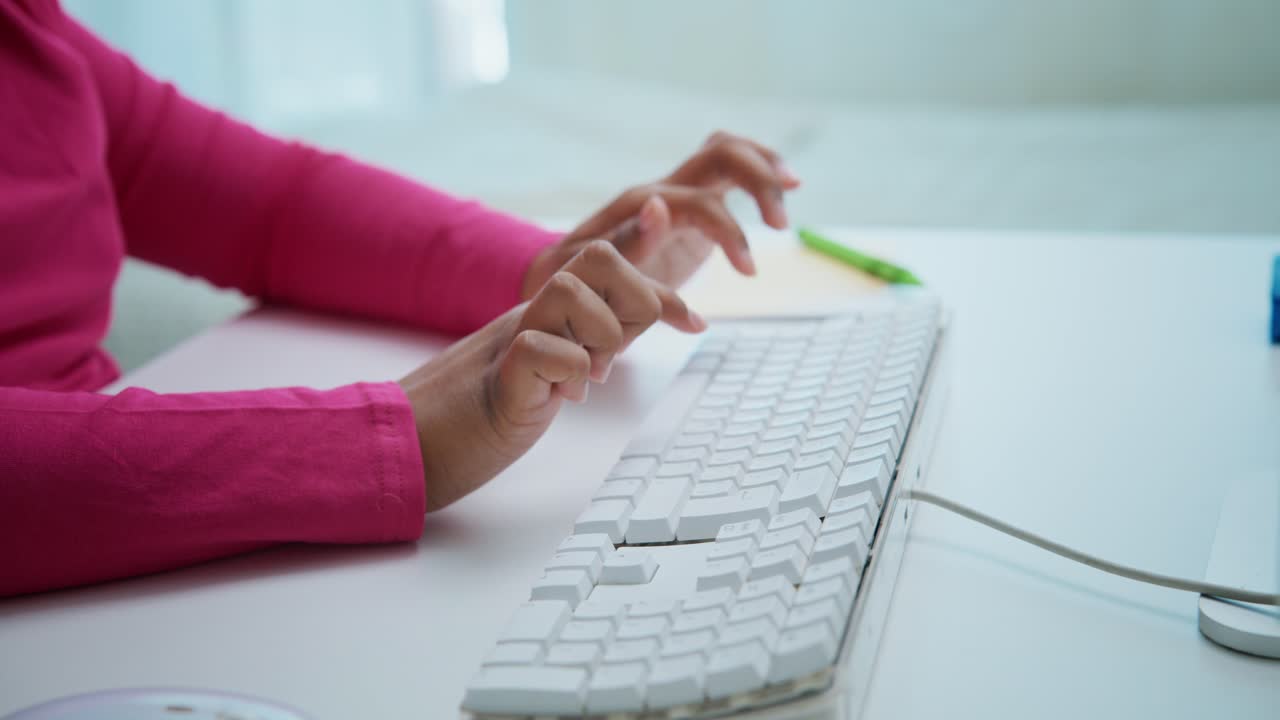 Professional female worker wearing pink shirt rapidly typing on white keyboard at clean, modern workspace, focusing on digital task with quick, precise hand movements