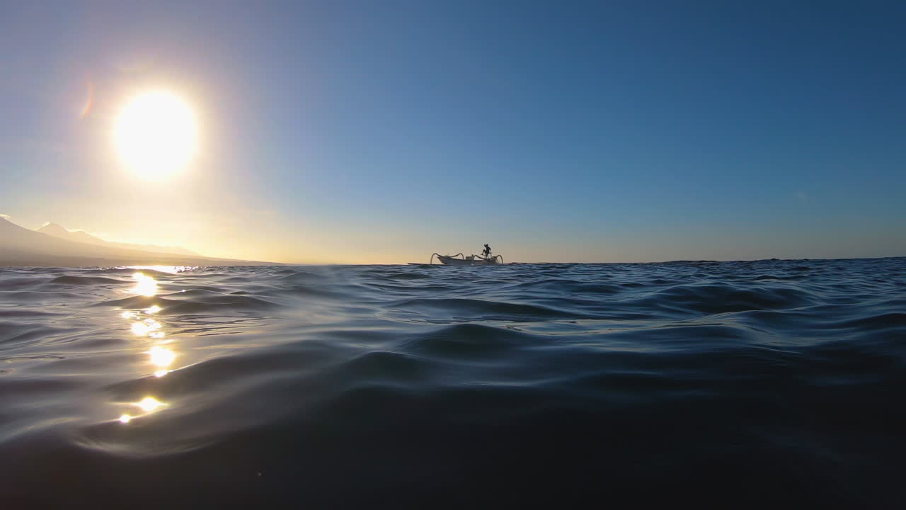 Underwater transition to above water with passing fishing boat and a mountain in the sunset distance.