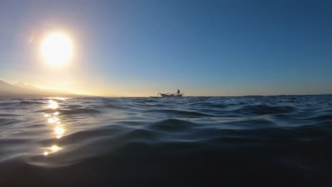 underwater transition to above water with passing fishing boat and a mountain in the sunset distance.