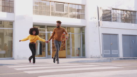 fashionable young black couple running across a city street holding hands, full length