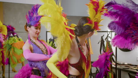 three pretty dancers with feather colorful dresses getting ready