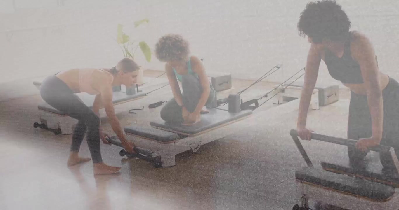 Instructor cueing, three women adjusting reformer footbar, carriage and mat for Pilates alignment