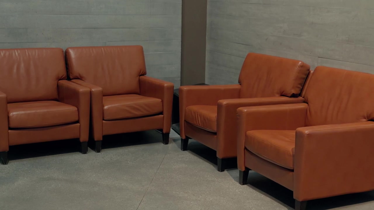 A right to left camera glide passes four brown armchairs against concrete walls.