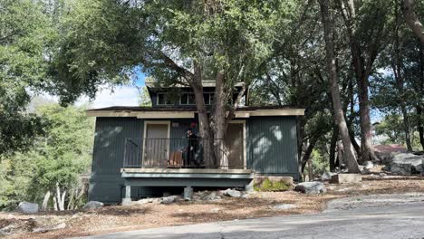 joven hombre caucásico con barba vestido de negro sentado en el porche de un dúplex verde en un bosque en el sur de california
