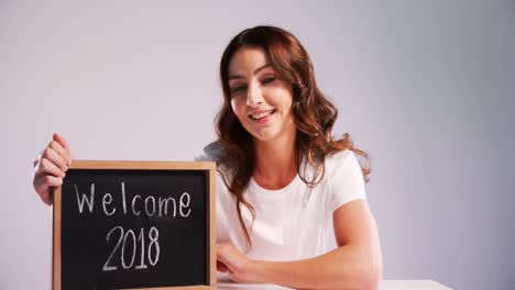 Portrait-of-smiling-woman-showing-slate-with-text-welcome-2018-4k