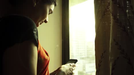 a beautiful indian woman also stands by the window and uses her smartphone...
