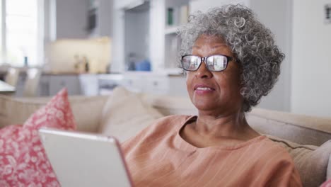 senior african american woman having a video chat on digital tablet while sitting on the couch at ho