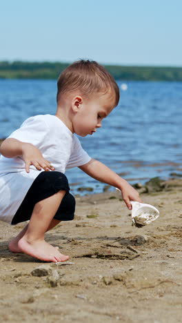 little caucasian boy in white t-shirt digging sand on the beach. toddler working with shovel on the shore. vertical video