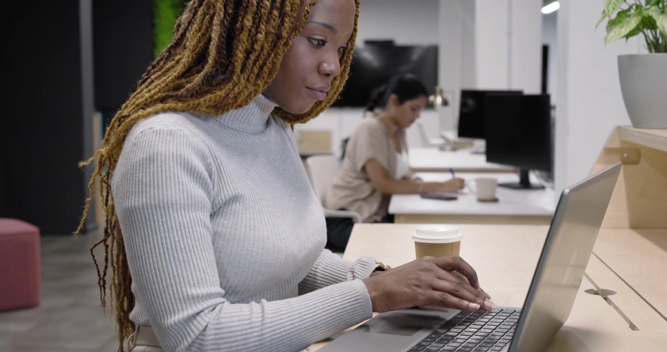 Mangfoldige kolleger, afroamerikansk kvinde i gråt taster på bærbar computer, arbejder ved skrivebord nær kaffekop