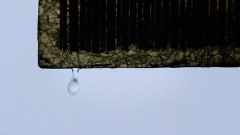 close-up shot of rain droplet falling from corner of roof shade during rainy weather with soft light