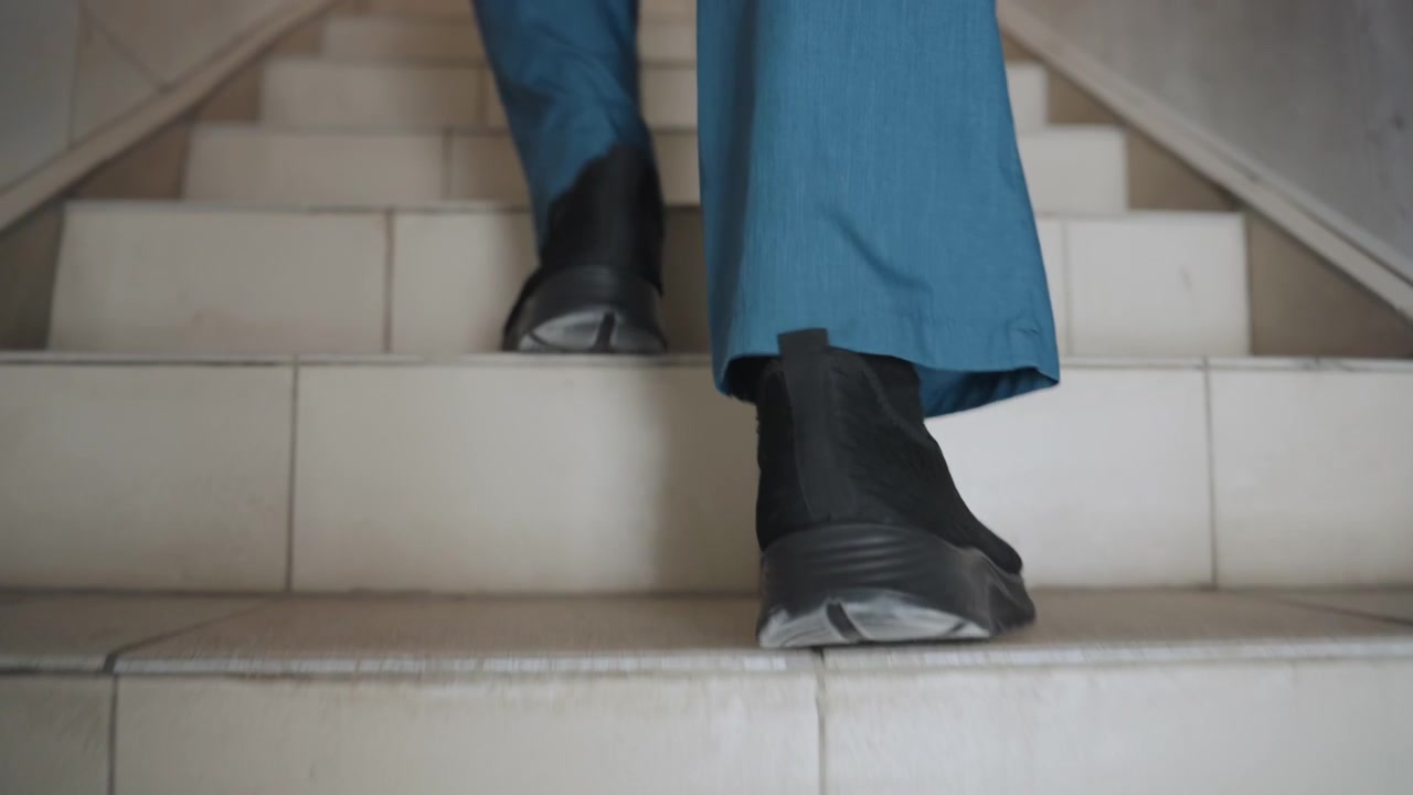 White paramedic ascending tiled stairs with urgency, closeup on black soles and traction, quick purposeful strides in blue scrubs, heel and toe motion highlighted, approach toward landing and doorway