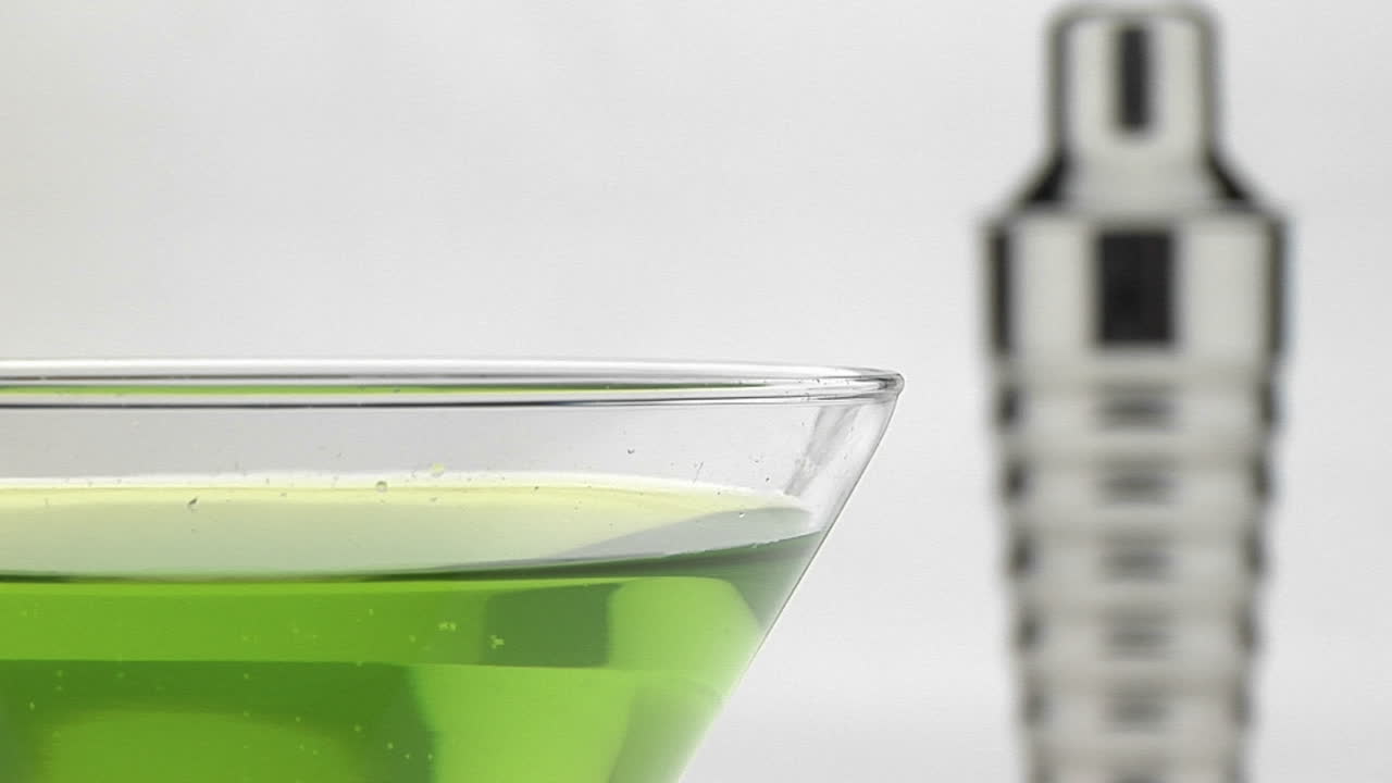 una coctelera de martini plateada se sienta detrás de un vaso con líquido verde dentro