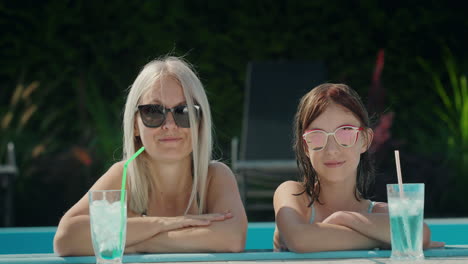 portrait of a mother with her daughter, relaxing in the pool. cooling drinks are next to them. looking at the camera