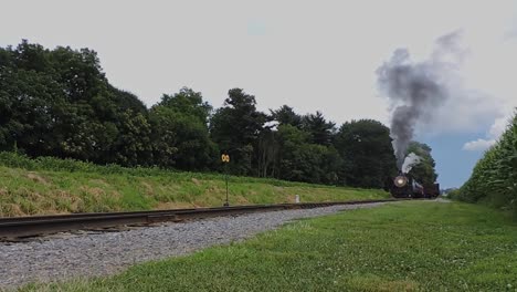 a low angle of a steam passenger train starting up with puffs of smoke and steam on a sunny day