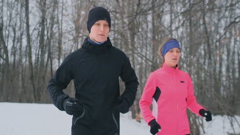 Young-family-couple-man-and-woman-on-a-morning-jog-in-the-winter-forest.-A-woman-in-a-loose-jacket-a-man-in-a-black-jacket-is-running-through-a-winter-park.-Healthy-lifestyle-happy-family