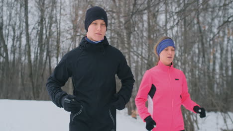 joven pareja familiar, hombre y mujer, corriendo por la mañana en el bosque de invierno. una mujer con una chaqueta holgada y un hombre con una chaqueta negra corre por un parque de invierno. estilo de vida saludable familia feliz