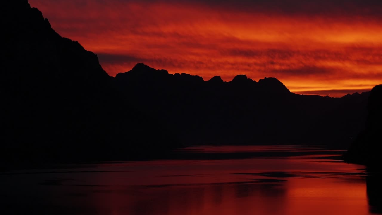 Fiery evening sky casts vibrant hues over Lake Walensee in Switzerland, with silhouetted mountains framing the serene waters. Capturing nature’s beauty at twilight.