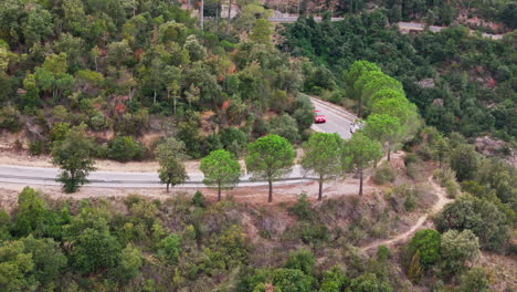 drone pan tiro capturando una carretera sinuosa, con coches con gracia pasando a través, flanqueado por árboles verdes exuberantes que surgen de las montañas