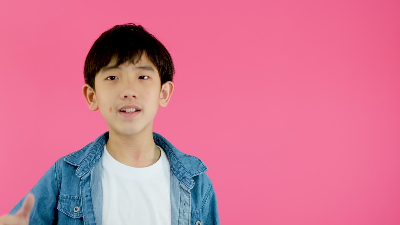 Young boy smiles and gives thumbs up, bright lighting, static camera, vibrant pink backdrop