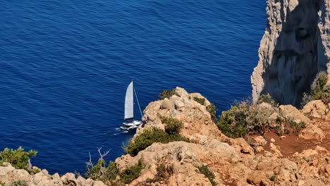 Un-Velero-Conduce-Sobre-El-Agua-Azul-En-Un-Hermoso-Día,-Antes-De-Esconderse-Detrás-De-Rocas,-Cámara-Lenta-Y-Espacio-Para-Copiar