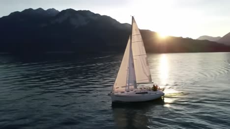 a lone sailboat glides across the serene waters of a lake as the sun sets behind majestic mountains. the peaceful atmosphere creates a perfect moment for reflection and enjoyment of nature.