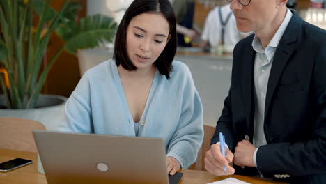 Una-Mujer-De-Negocios-Que-Muestra-Documentos-En-La-Computadora-Portátil-A-Un-Hombre-De-Negocios-En-Una-Reunión-En-Una-Cafetería