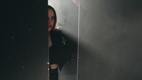 mysterious shot of a woman in black, half-hidden behind a wood partition with soft light illuminating her hand, zooming in