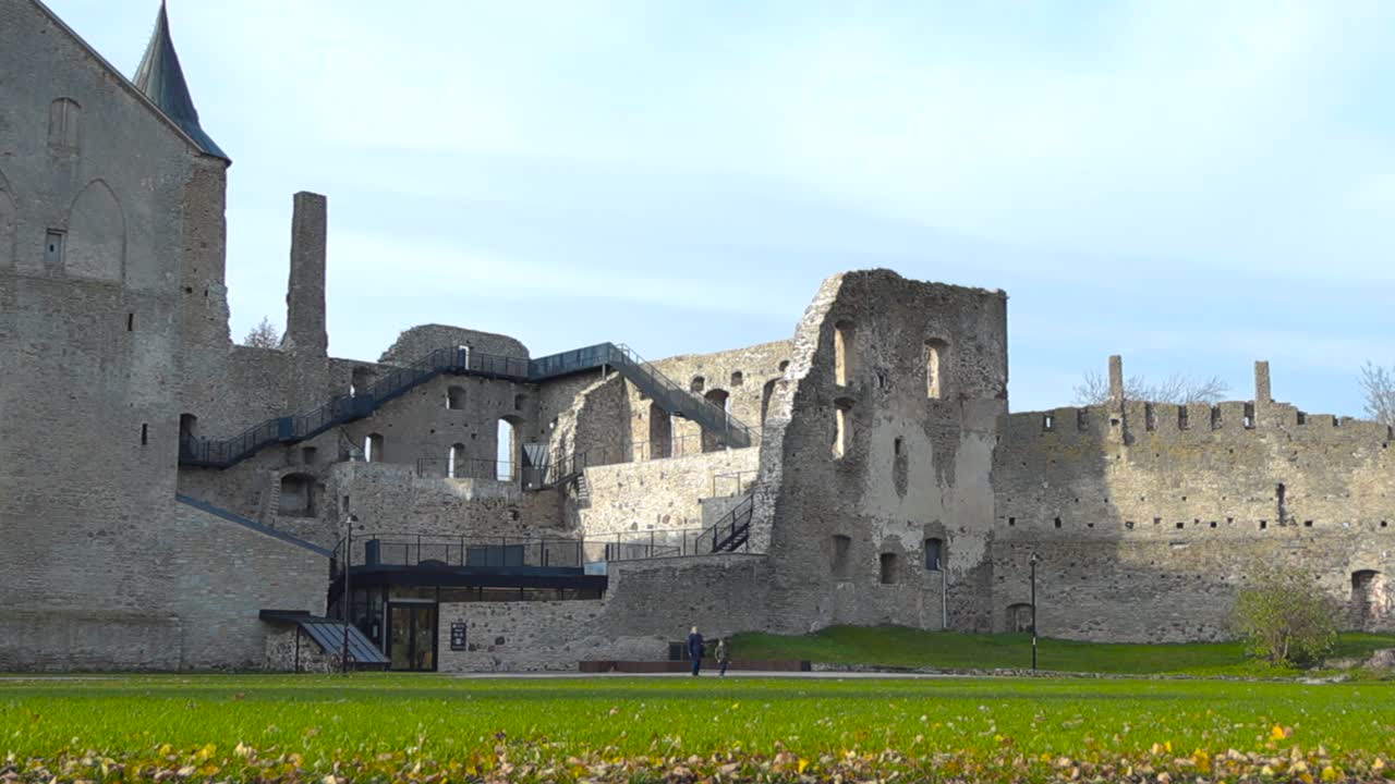 Low angle footage of Haapsalu castle medieval architecture limestone building during autumn or late summer while sun is shining. Sun is casting shadows on the falling apart fortress and blue sky seen.