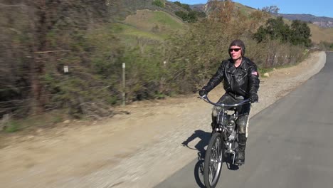 a man in leather jacket drives a motorized bicycle along a country road 3