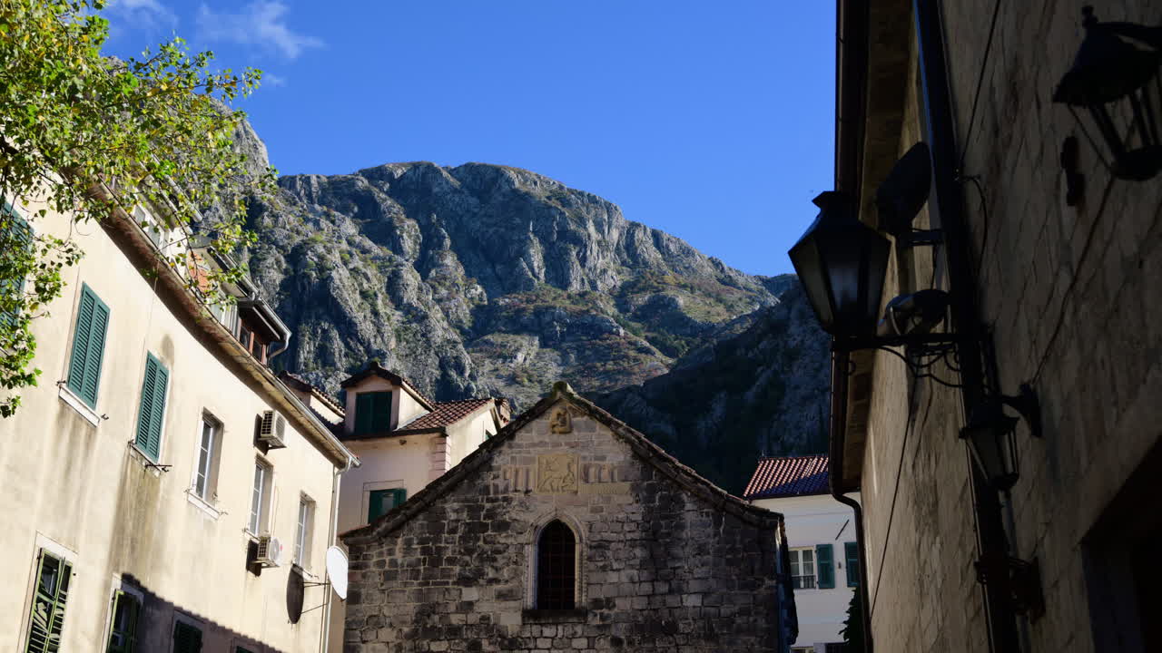 Mavi gökyüzü altında uzanan görkemli bir dağ sırası eşliğinde Kotor Eski Kenti'ndeki taş binalar