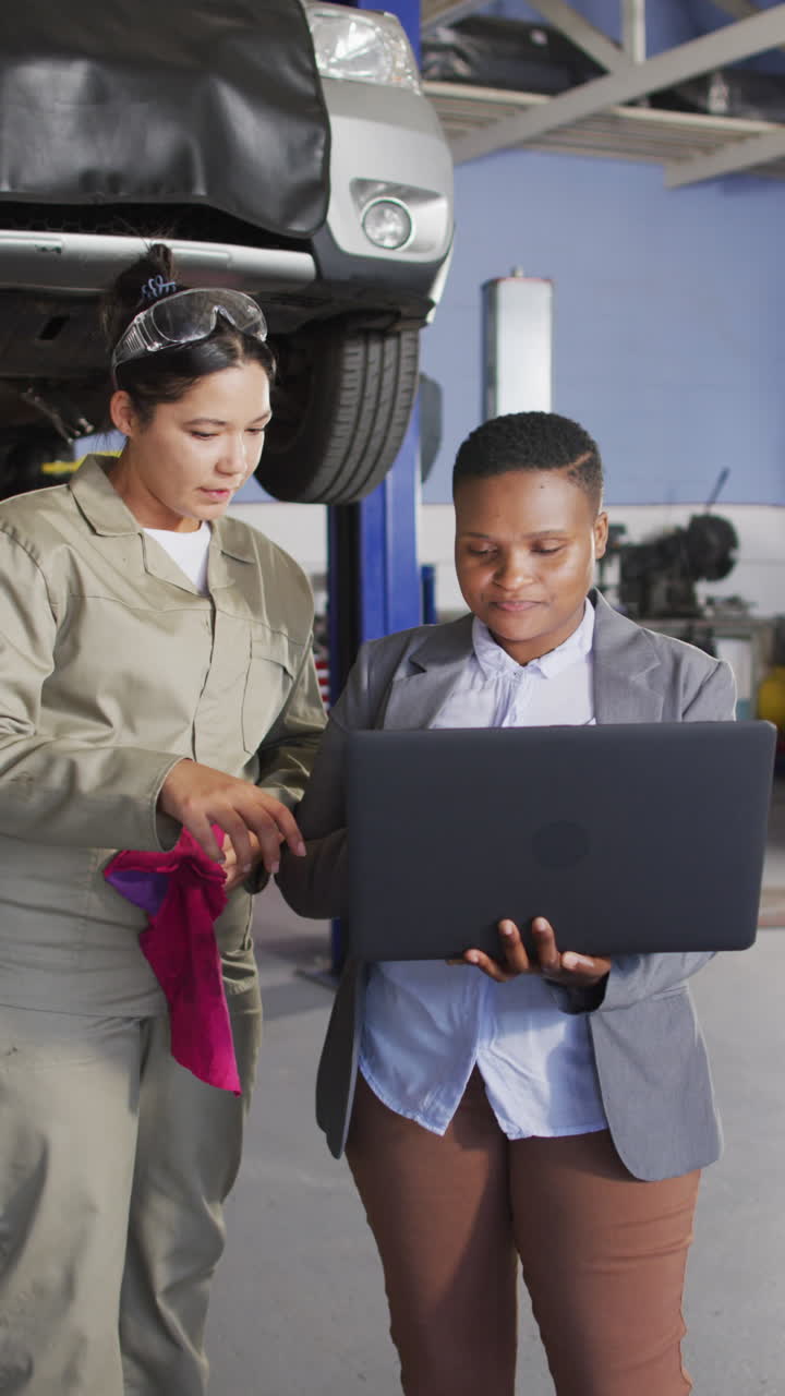 video vertical de dos mecánicas de automóviles femeninas diversas usando una computadora portátil