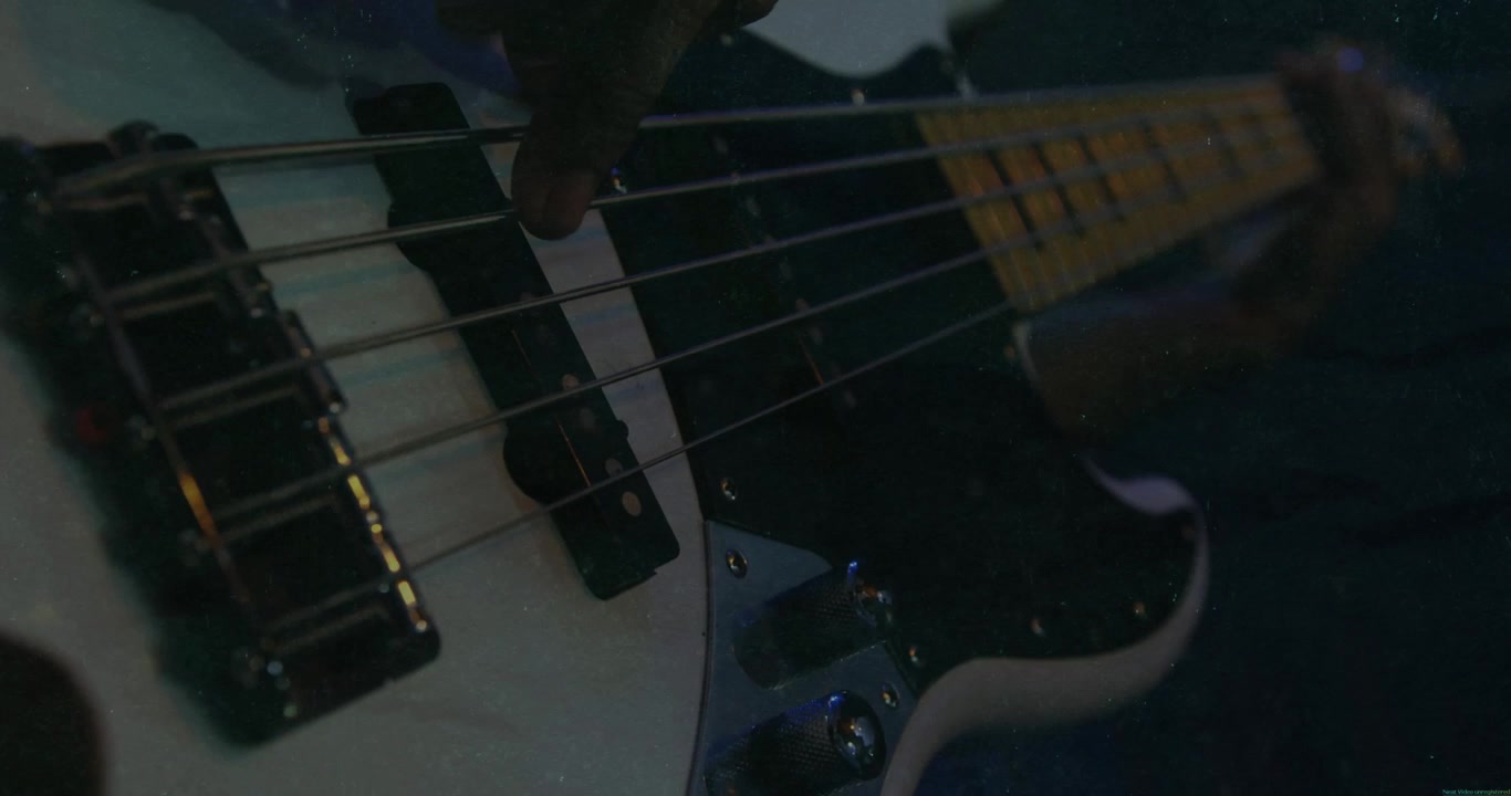 Mano di un musicista che si libra sopra le corde bianche di un basso, pizzicando le note e creando una linea di basso.
