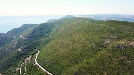 Breathtaking aerial view capturing a winding road along the lush slopes of Parque Natural da Arrábida, with the vast Atlantic Ocean stretching in the background, Portugal