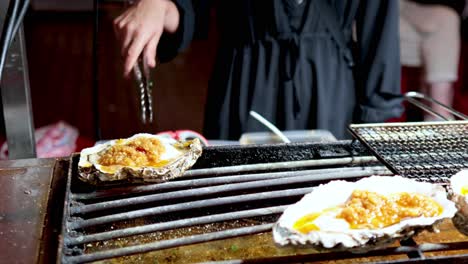 ostras siendo sazonadas y asadas por un chef
