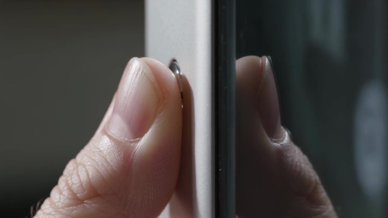 Approaching hand pinching metal loop on phone edge on desk near glossy surface, securing ring